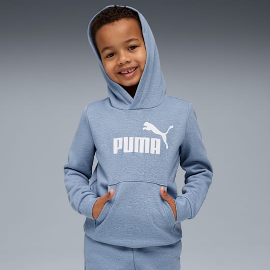 A child smiles against a grey backdrop, wearing a blue hooded top with a white logo.