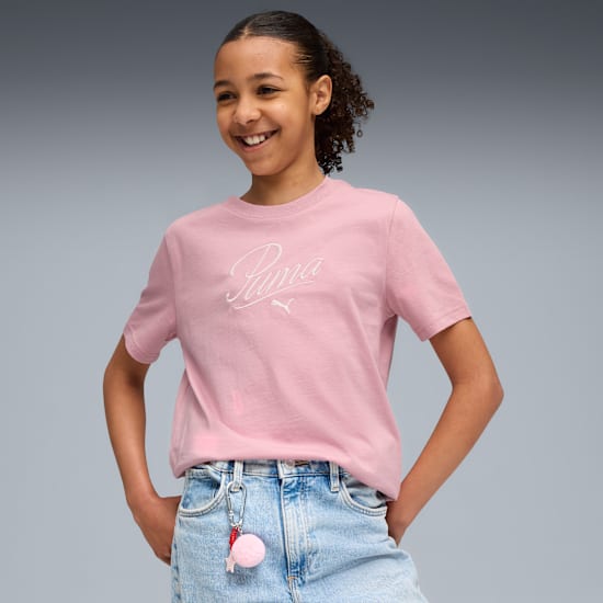 Ein lächelndes Model posiert vor grauem Hintergrund, mit rosa T-Shirt und Jeans.