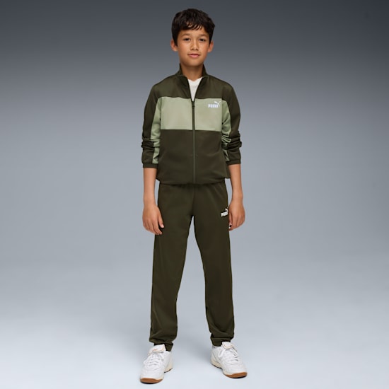 A model stands against a grey backdrop, wearing a green tracksuit and white trainers.