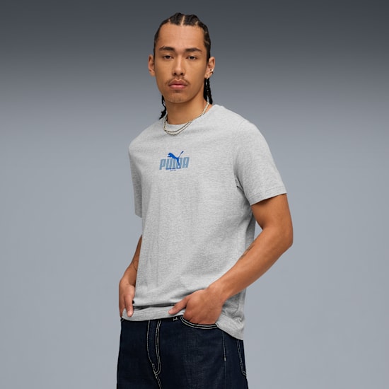 Sur fond gris, un mannequin pose en t-shirt gris, avec un logo bleu et un jean foncé.