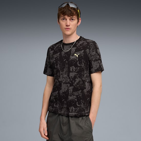 A model poses against grey backdrop, wearing a patterned t-shirt and dark shorts.