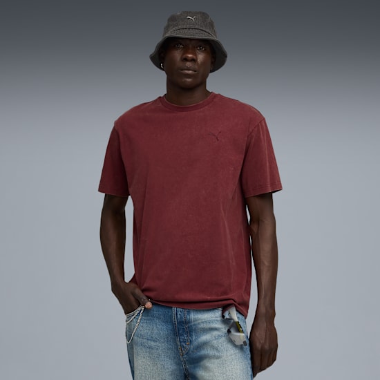 Un modello posa su sfondo grigio, con cappello, t-shirt bordeaux e jeans blu.