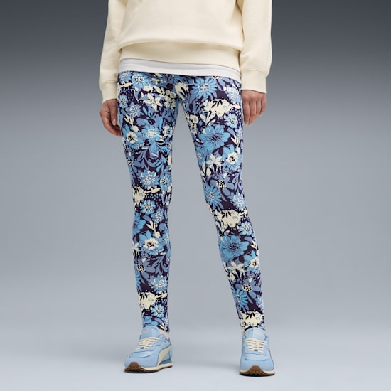 Ein Model vor grauem Hintergrund, mit floralen Leggings und blauen Turnschuhen.