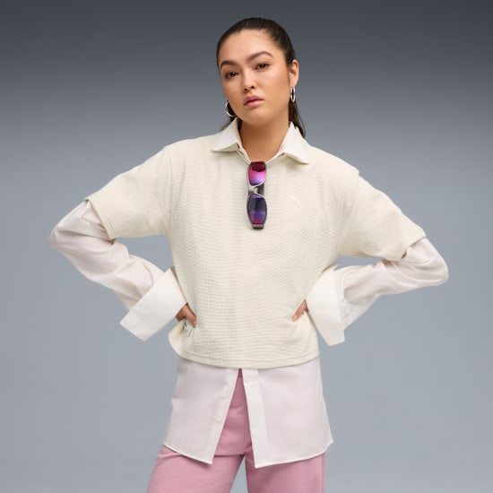 A model with hands on hips poses in front of a grey background wearing pink trousers.