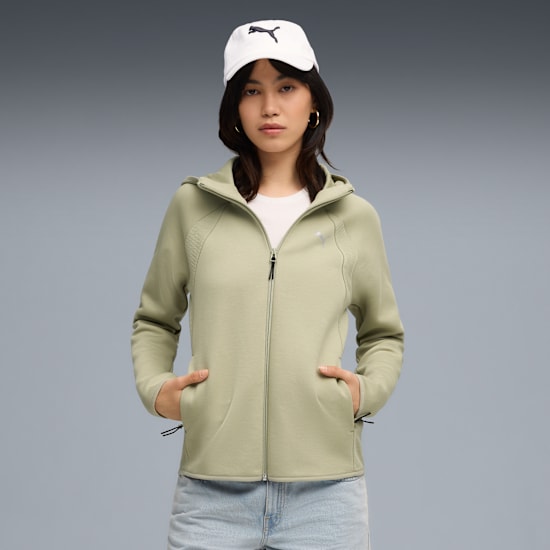 On grey, a model poses in a white cap, light green hooded jacket, and light blue jeans.