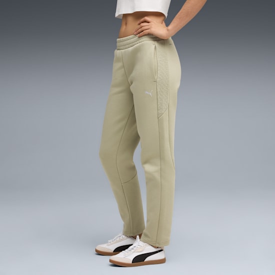A model poses on grey wearing cream trousers and trainers with a white top.
