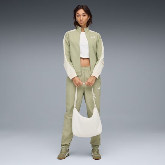 Model vor grauem Hintergrund, trägt Trainingsanzug und hält eine weiße Tasche.