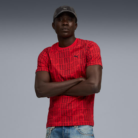 A model with crossed arms wears a red patterned t-shirt against a grey background.