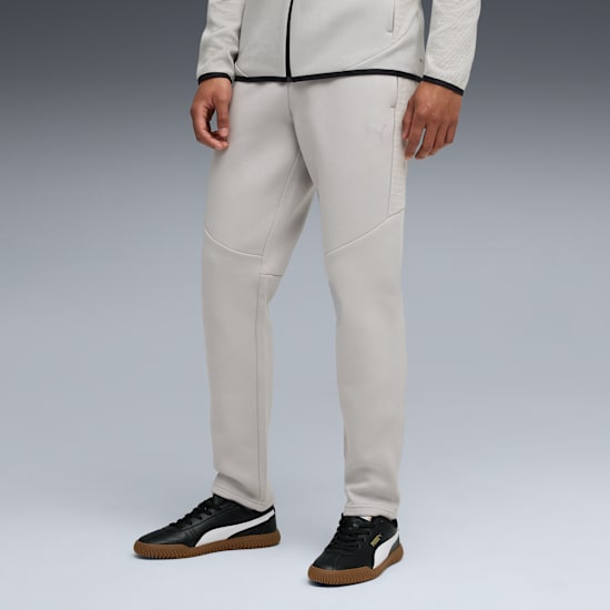 Op grijs poseert een model in een lichte broek en zwarte sportschoenen met bruine zolen.