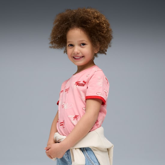 Un enfant souriant aux cheveux bouclés porte un t-shirt rose à motifs sur fond gris.