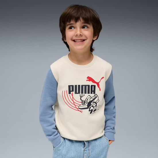 A smiling child poses in front of a grey background wearing a Puma branded top.