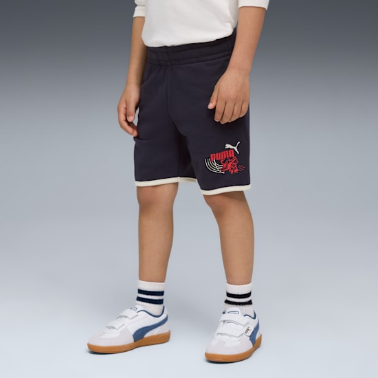 Op grijs toont een kind een marineblauwe short met logo, gecombineerd met gestreepte sokken en klittenbandschoenen.