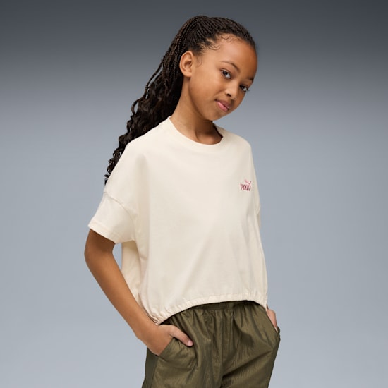 A model poses on a grey backdrop, wearing a cream top and khaki trousers.