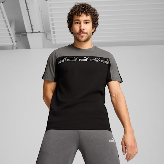 Vor grauem Hintergrund posiert ein Model in einem schwarz-grau-weißem Logo-T-Shirt.