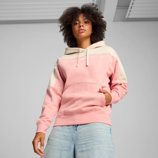A model poses against grey, wearing a pink and cream hoodie and light blue denim shorts.