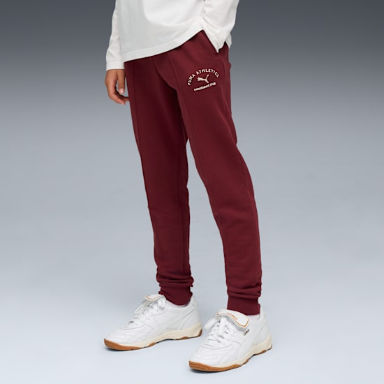 Su sfondo grigio, un modello indossa top bianco, pantaloni da jogging bordeaux con logo e scarpe da ginnastica bianche.