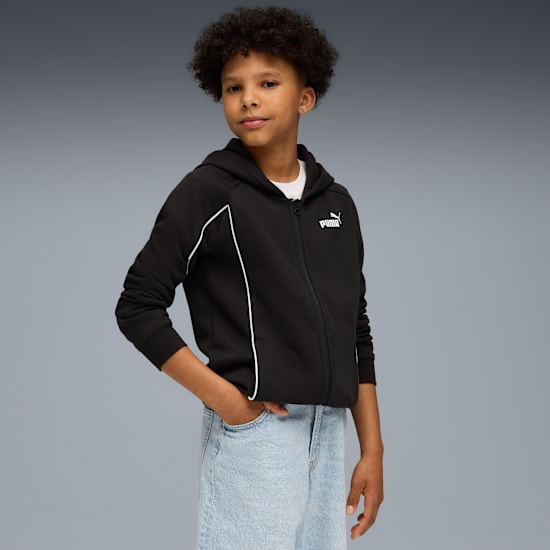 A child poses against grey wearing a black Puma zip-up hoodie and light blue jeans.