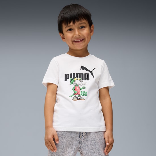 A smiling child poses against grey, wearing a white Puma t-shirt with a cartoon.