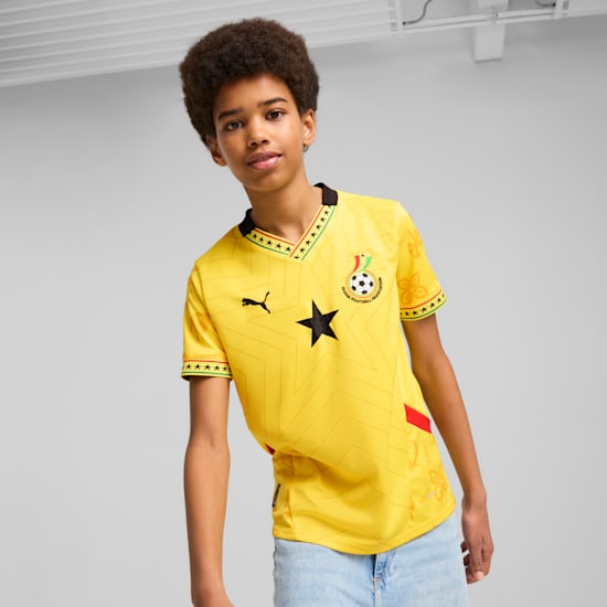 Model wears a yellow Ghana football shirt against a grey backdrop.