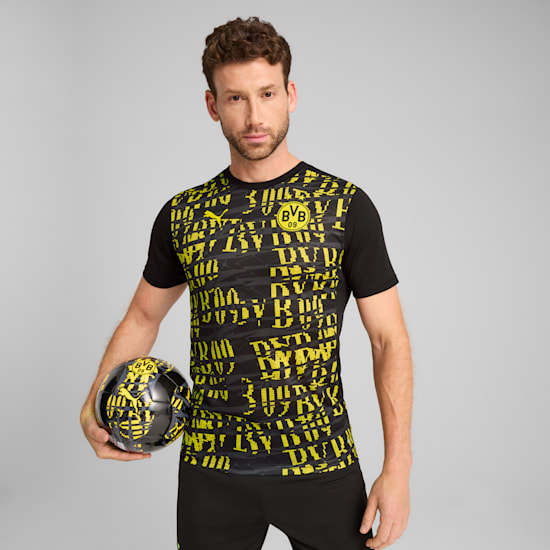 Against a grey backdrop, a model holds a football wearing a black and yellow BVB shirt.
