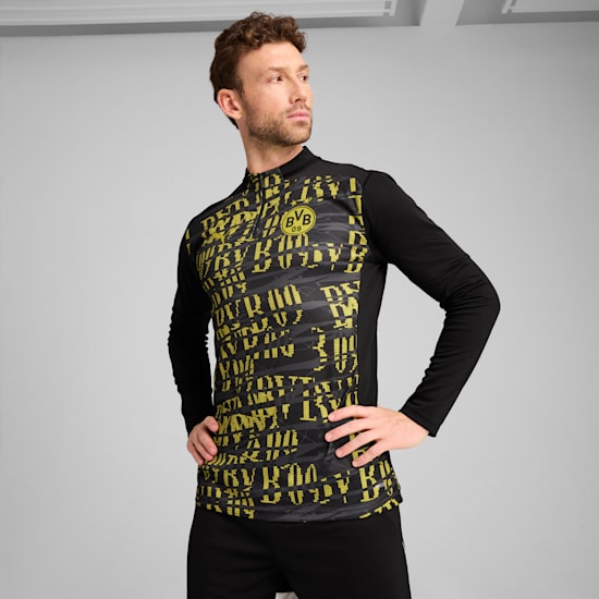 Tegen een grijze achtergrond poseert een model in een zwart-gele BVB-trainingstop.