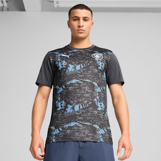 A model stands against a grey backdrop, wearing a patterned black and blue t-shirt and navy shorts.