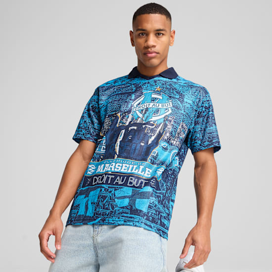 A model in front of a grey background is wearing a patterned blue t-shirt and light blue jeans.