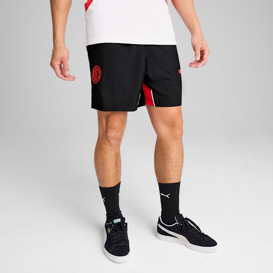 Tegen een grijze achtergrond draagt een persoon een witte top, zwarte shorts en sportschoenen.