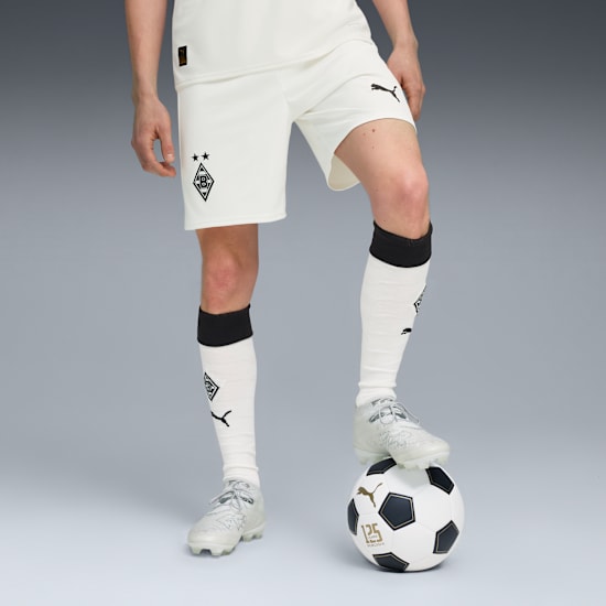 Auf Grau posiert ein Model in weißem Trikot mit einem Fuß auf einem schwarz-weißen Fußball.