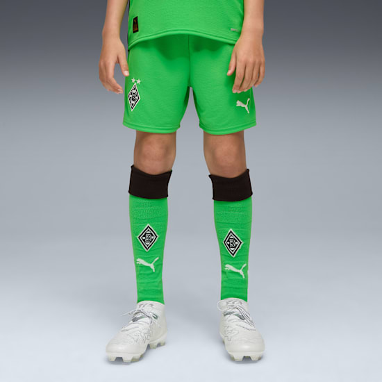 A model stands against grey wearing a green kit with socks and white football boots.