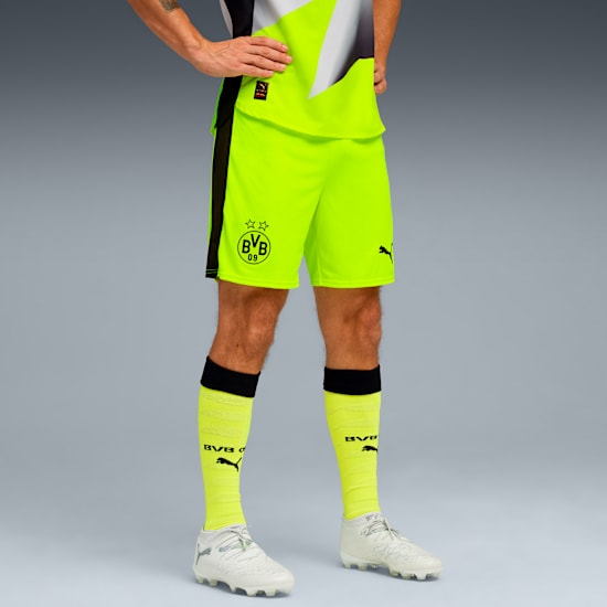 A model poses against grey wearing a yellow and black sports kit with white shoes.