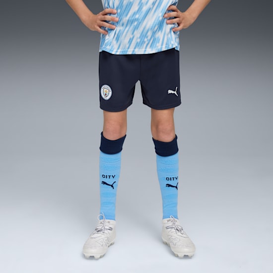 A model with hands on hips, wearing a football kit with blue socks and white trainers.