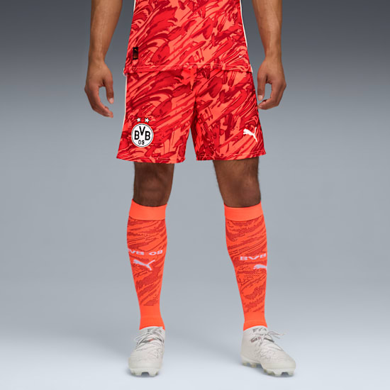 Model on grey backdrop wears patterned red shorts, socks and trainers.