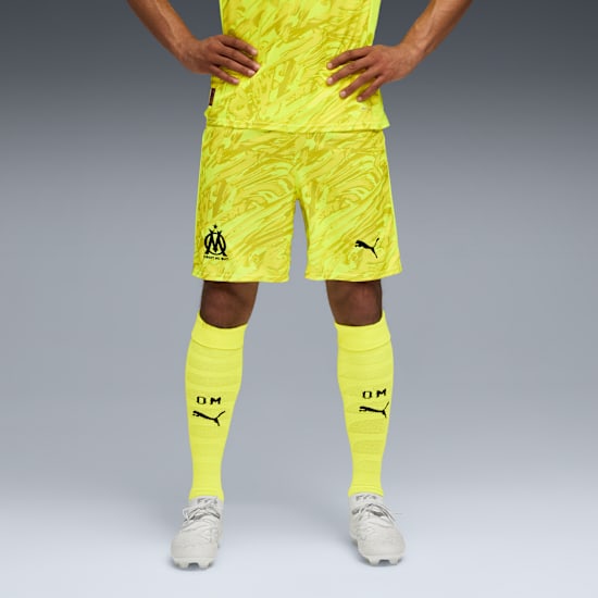 Against grey, model displays yellow patterned shirt, shorts, socks and white trainers.