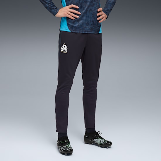 Su sfondo grigio, un modello indossa pantaloni scuri con logo e top fantasia.