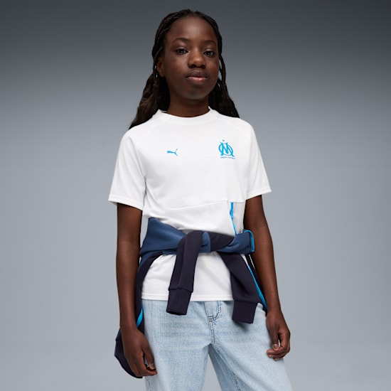 Tegen grijs draagt een model een wit T-shirt met logo's en een jas om de middel.