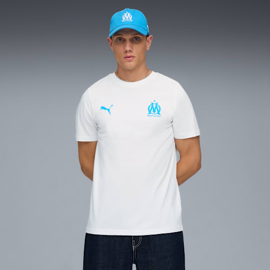 A model poses against a grey backdrop wearing a white t-shirt, jeans, and a blue cap.