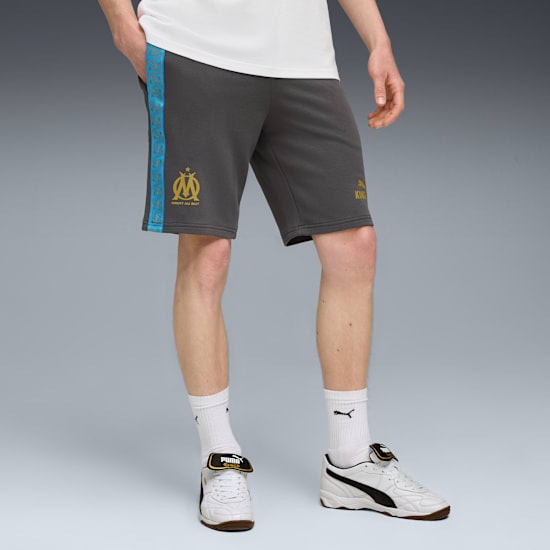 On grey, a model wears grey shorts with logos, a white t-shirt, socks and white trainers.