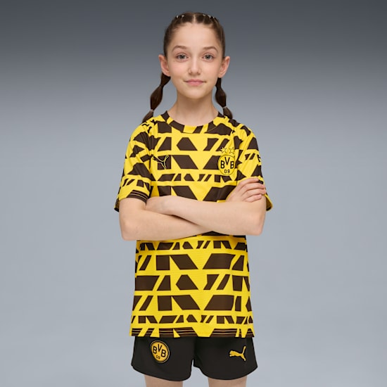 A girl with pigtails stands against a grey background, arms crossed, wearing BVB patterned sportswear.