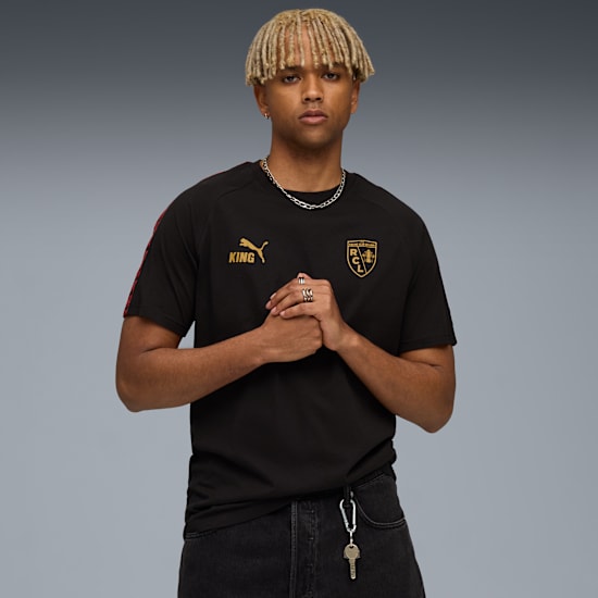 Against a grey backdrop, a model wears a black t-shirt and dark jeans.