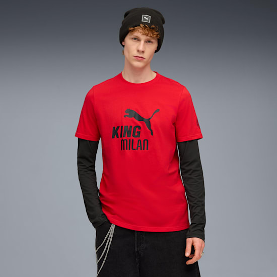 A model stands against grey wearing a beanie, red t-shirt, long sleeve top and dark trousers.