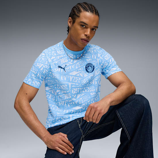 Op grijs, een model knielt met een lichtblauw shirt met patroon en een donkere jeans.