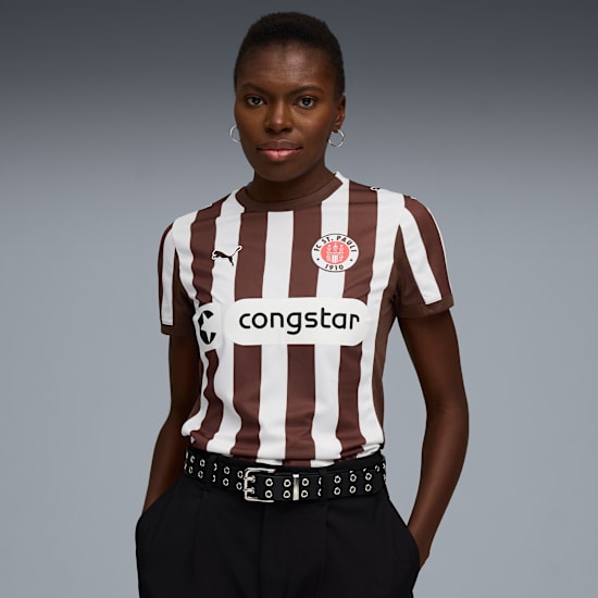 A model poses against grey wearing a brown and white striped shirt, and black trousers.
