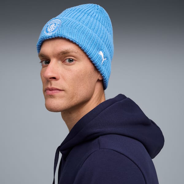A model with blue eyes wears a light blue beanie and a dark blue hoodie, against a grey backdrop.