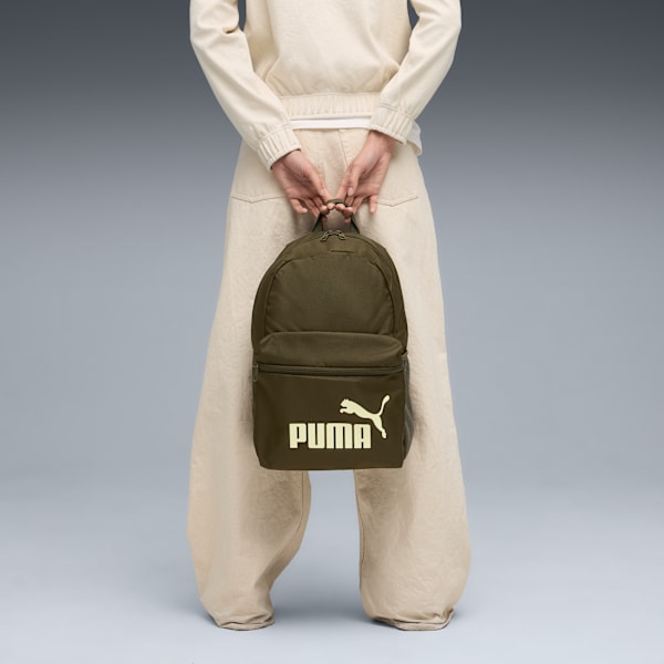 Against grey, a person holds an olive Puma bag with a cream logo, wearing beige clothing.