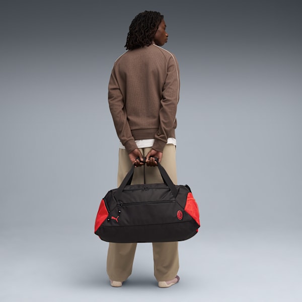 Against a grey backdrop, a model holds a black and red duffel bag, facing away from the camera.