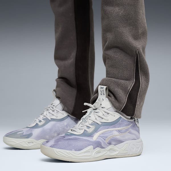 Against grey, a model wears grey joggers and patterned trainers in a walking pose.