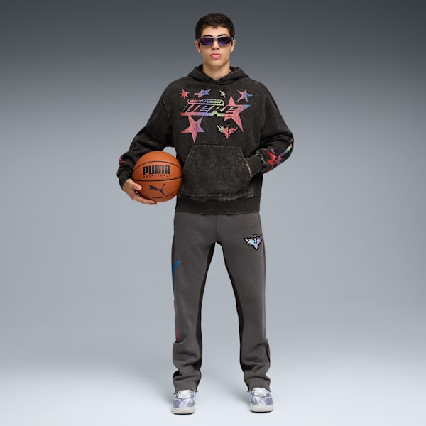 A model with sunglasses in front of a grey backdrop holding a basketball, wearing a hoodie and joggers.