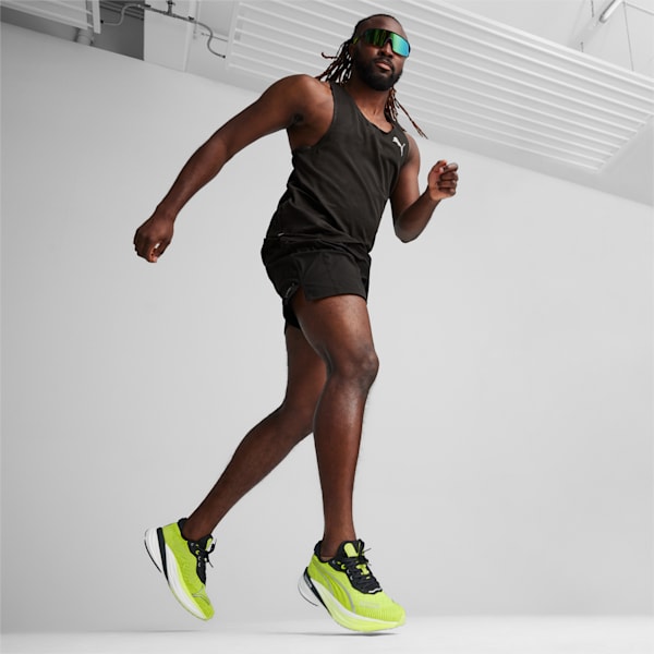 A model runs against a grey backdrop, wearing a black tank top, shorts and neon trainers.
