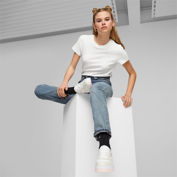 On grey, a model poses on a white cube wearing jeans, tee, and platform trainers.